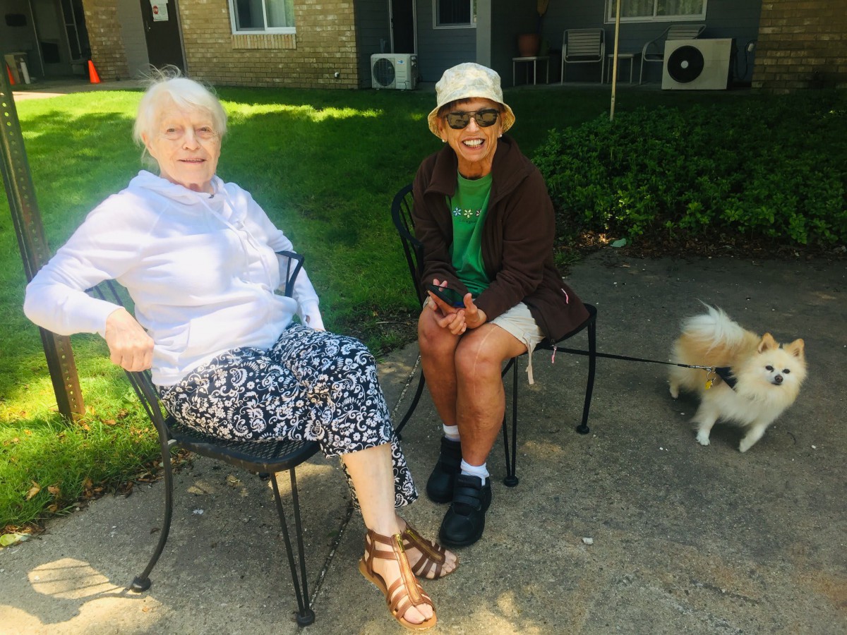 Two people sitting outside with a small dog on a sunny day.