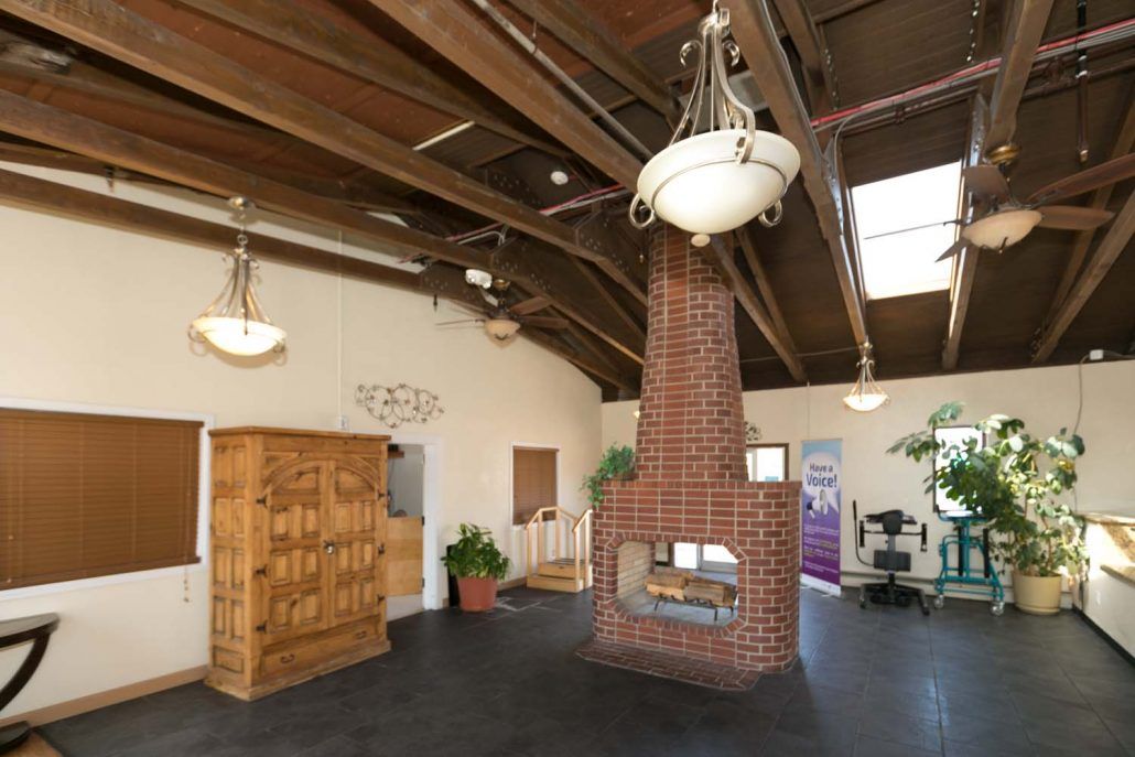 A spacious interior featuring a rustic brick fireplace, exposed wooden beams, and elegant chandeliers.