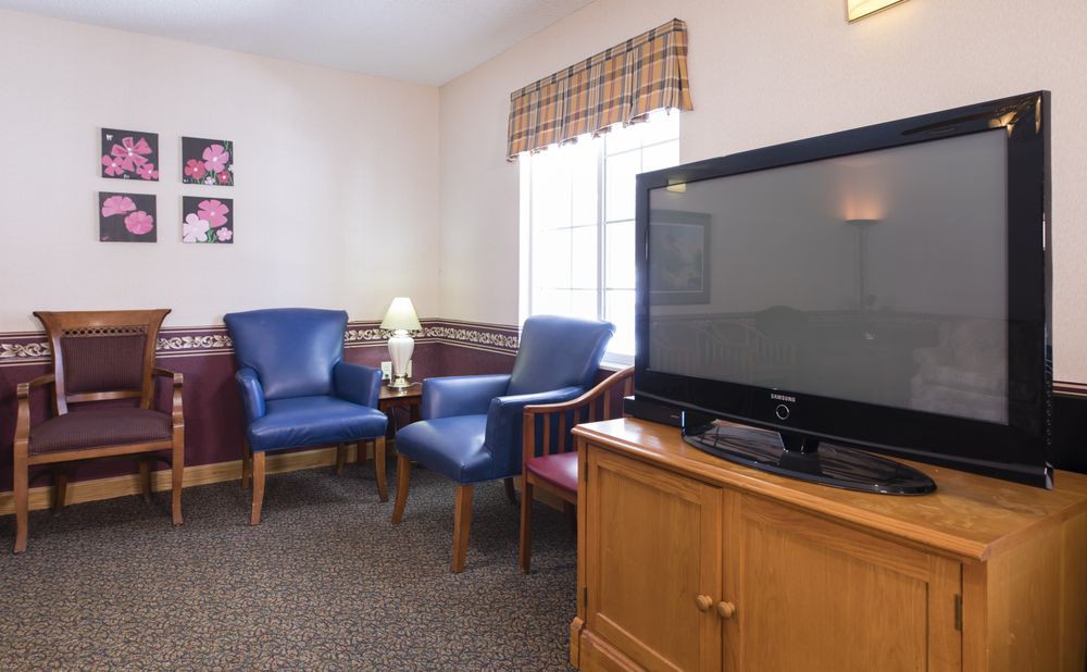 A cozy living room with blue chairs, a television on a wooden stand, and a window with curtains.