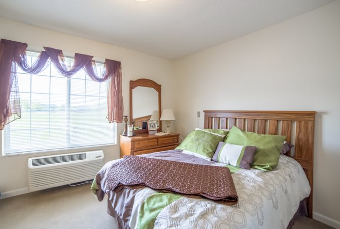 A cozy bedroom with a double bed, dresser, and large window letting in natural light.