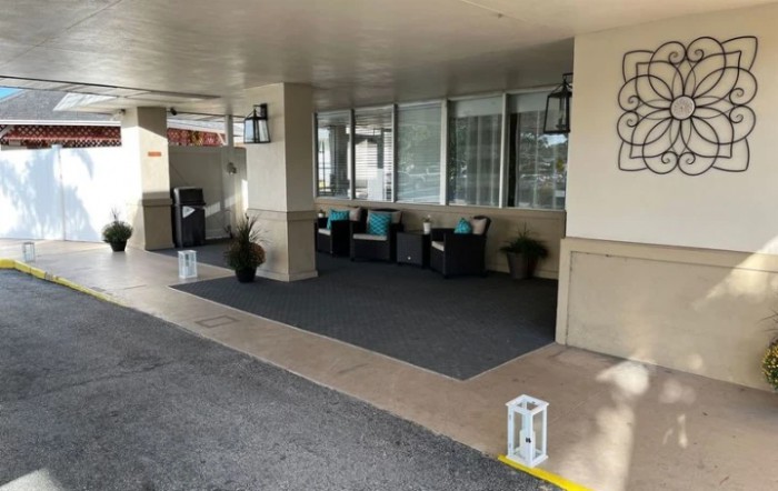 A cozy outdoor seating area near a building entrance, featuring cushioned chairs, lanterns, and decorative plants.
