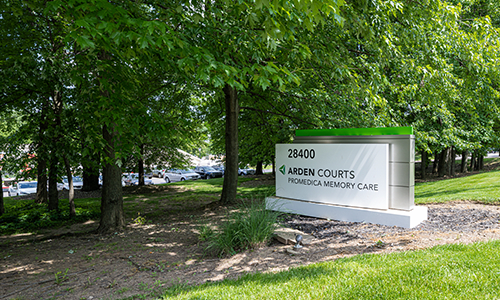 A sign for Arden Courts Memory Care facility surrounded by trees.