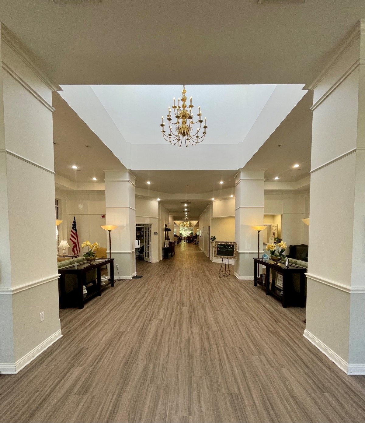 A spacious lobby with a chandelier and wood flooring, leading to a hallway.