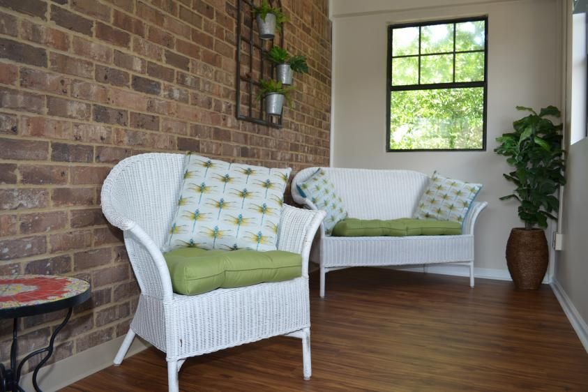 A cozy indoor seating area with wicker chairs and green cushions against a brick wall.