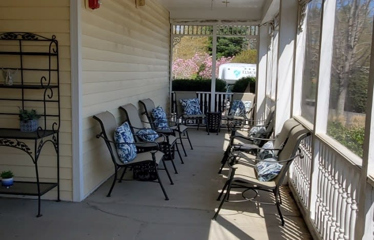 Outdoor porch with several chairs and cushions arranged in a row.
