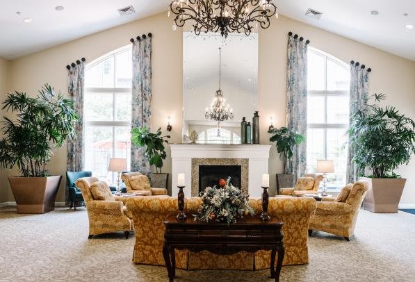 A spacious living room with elegant furnishings, featuring a central fireplace and a grand chandelier.