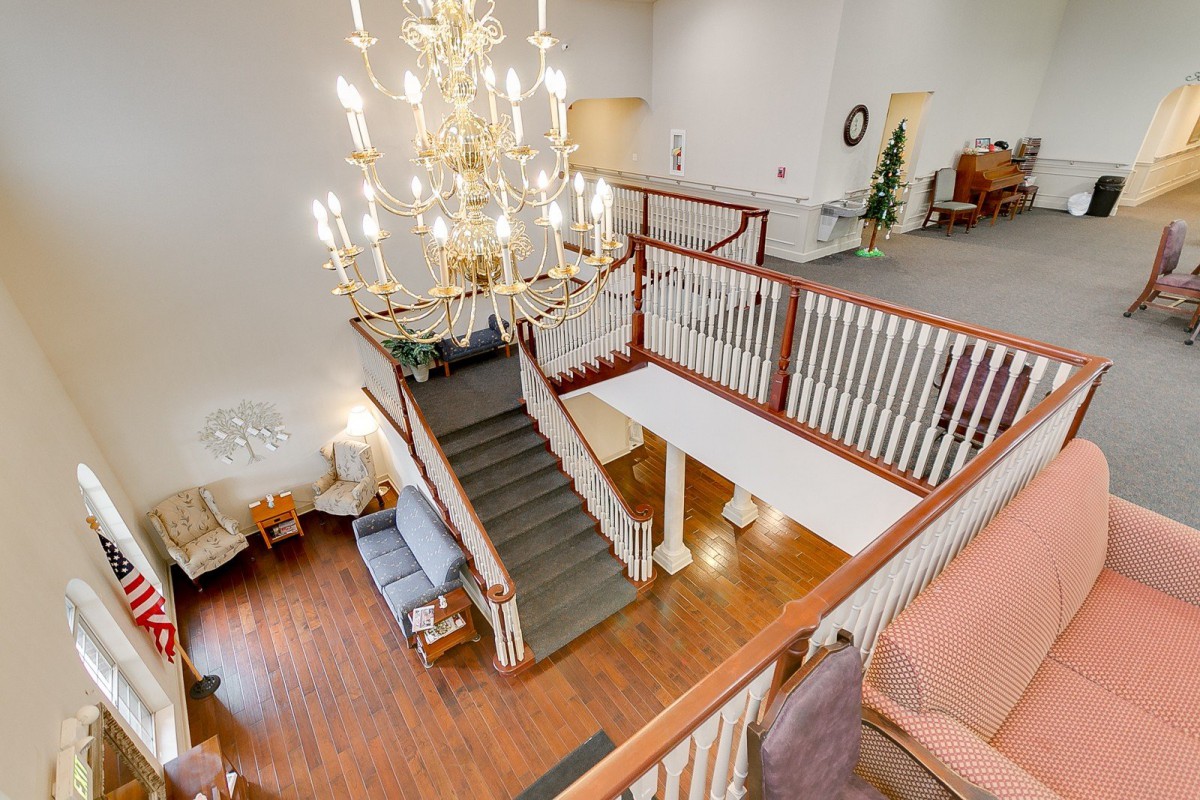 A well-lit lobby featuring a grand chandelier and a wooden staircase.