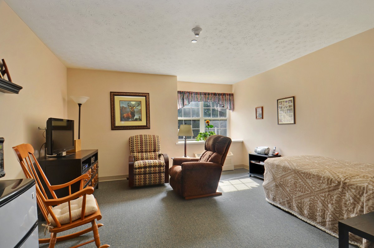 A cozy bedroom with a bed, chairs, and a window allowing natural light.
