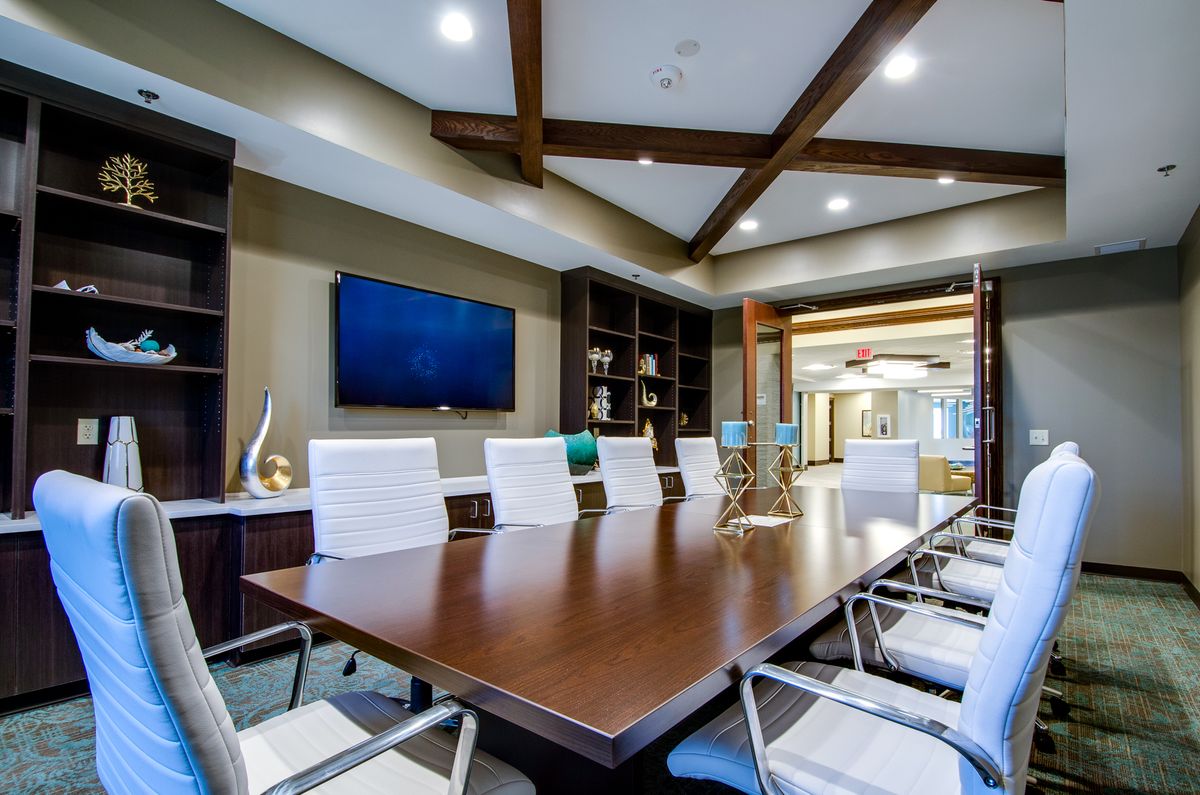 A modern conference room with a large meeting table, white chairs, and a wall-mounted TV screen.