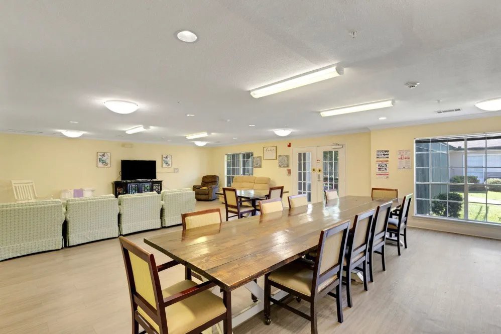 A spacious common room with a large dining table, chairs, and a seating area with couches and a television.
