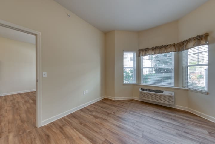 A bright empty room with hardwood floors and two large windows letting in natural light.