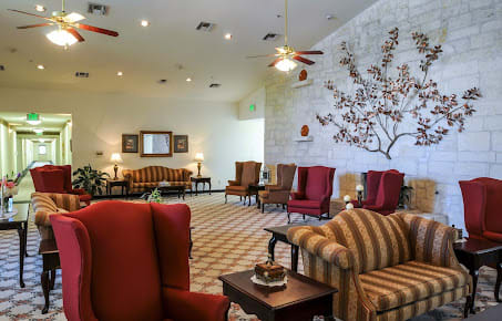 A spacious lobby with comfortable seating, featuring armchairs and a sofa, adorned with decorative elements and ceiling fans.