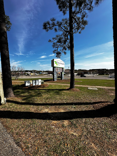 A view of a business sign surrounded by trees and open grass under a clear blue sky.