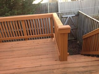 A wooden deck with railing and stairs leading to a fenced backyard.