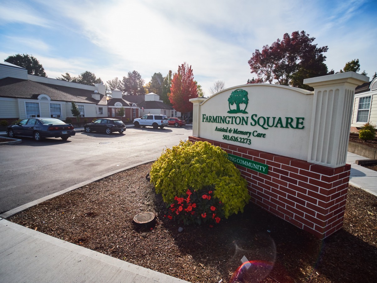 Entrance to Harrington Square Care, featuring a sign and landscaped parking area on an autumn day.