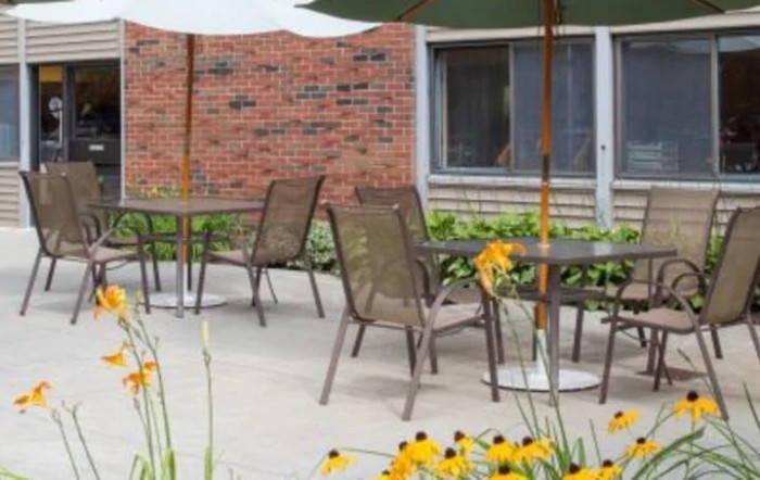 A cozy patio area with tables, chairs, and an umbrella surrounded by blooming flowers and a brick wall.