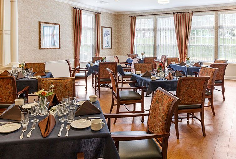 A well-arranged dining room with tables set for guests, featuring elegant tableware and warm lighting.