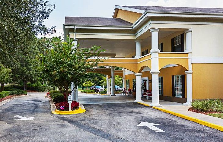 A yellow hotel building with columns and a landscaped driveway.