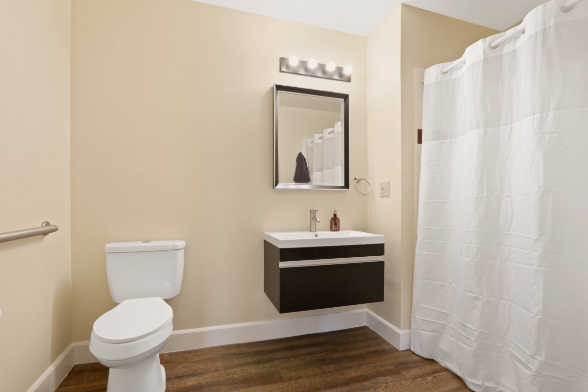 A modern bathroom with a wall-mounted sink, framed mirror, and shower curtain.