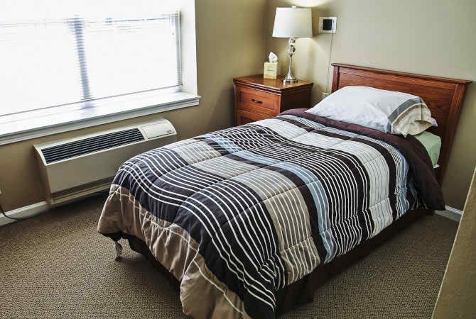 A cozy bedroom featuring a single bed with a striped blanket and a nightstand with a lamp.