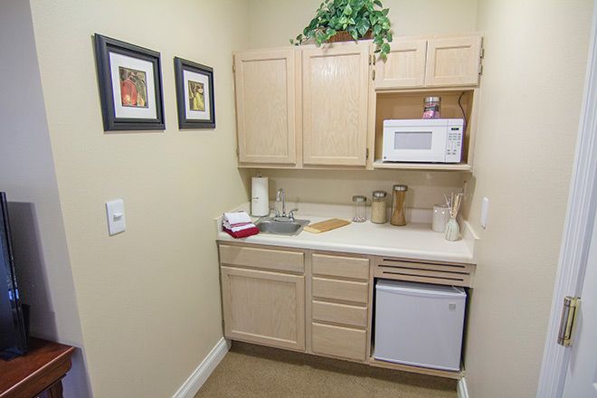 A small kitchenette with light wood cabinets, a microwave, mini fridge, and countertop decor.