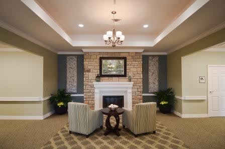A cozy living room with a fireplace, striped chairs, and a chandelier.