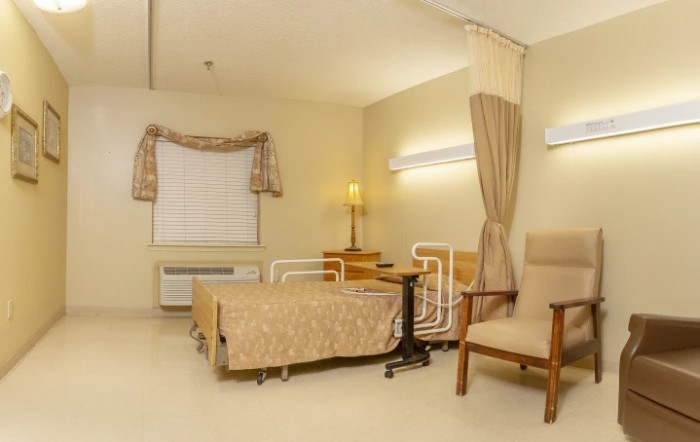 A clean and well-lit hospital room with a bed, chair, lamp, and curtain.
