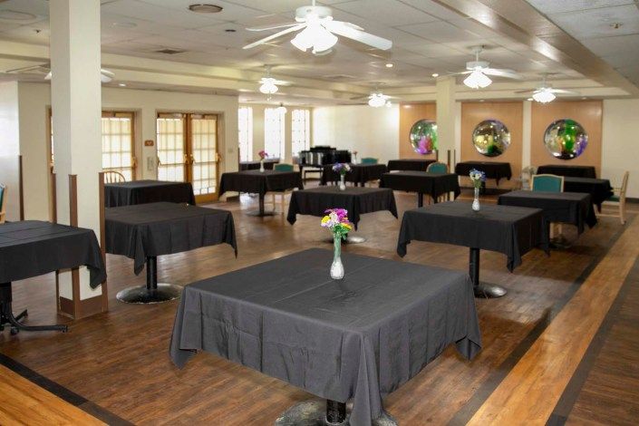 A banquet hall set up with tables covered in black tablecloths, each adorned with a vase of flowers.