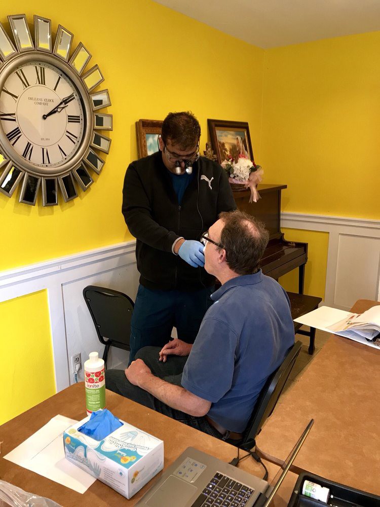 A healthcare professional examines a patient in a clinic room with a yellow wall.