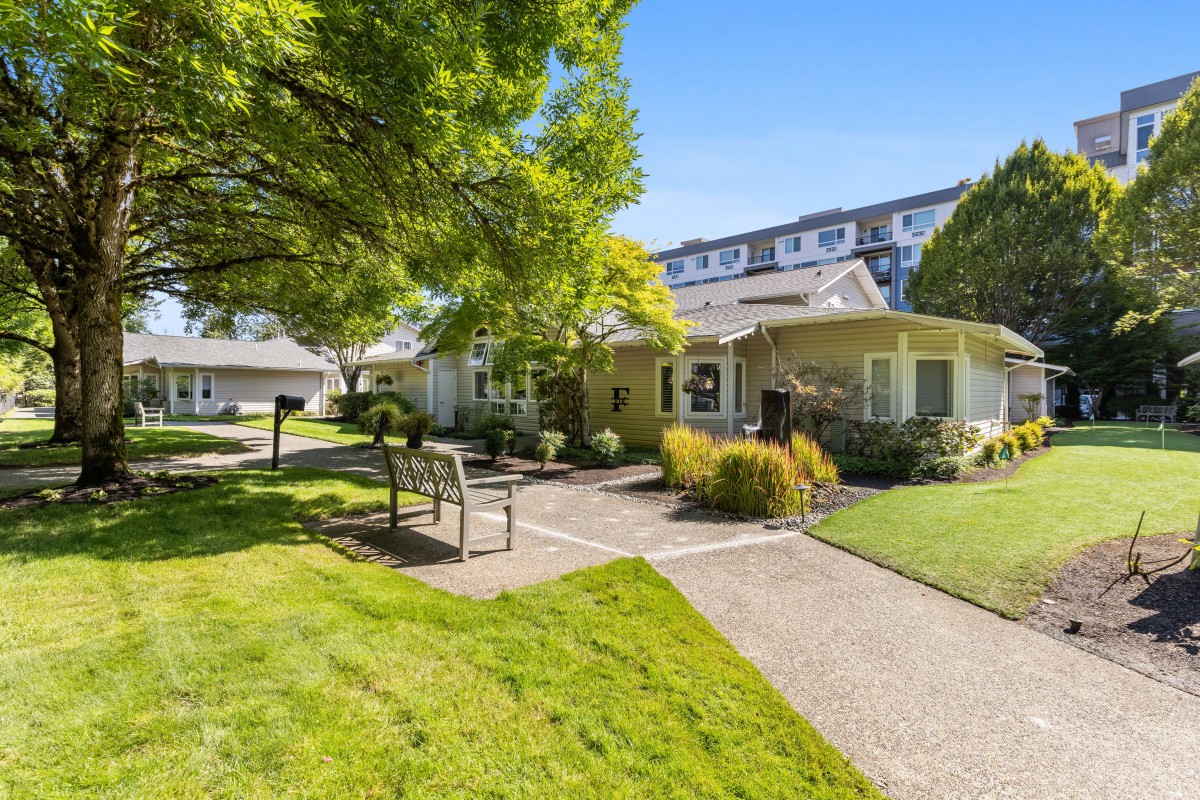 A well-maintained garden area with a pathway and benches in front of a residential building on a sunny day.