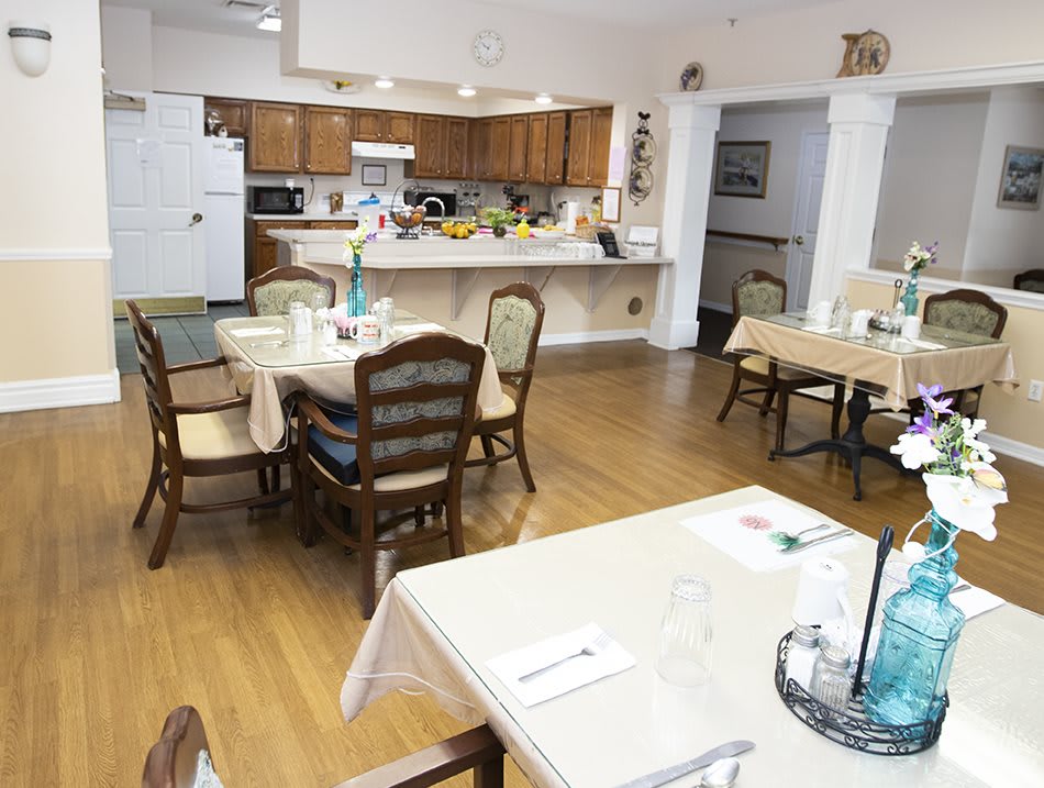 A cozy dining area with a connected kitchen, featuring tables and chairs set for dining.