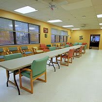 A spacious dining area with long tables and a variety of chairs, illuminated by bright overhead lights.