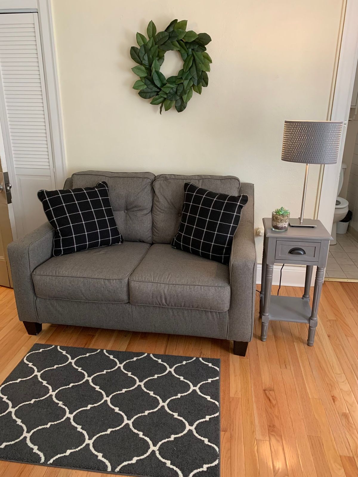 Cozy living room corner with a gray sofa, black patterned pillows, a small side table, and a lamp.