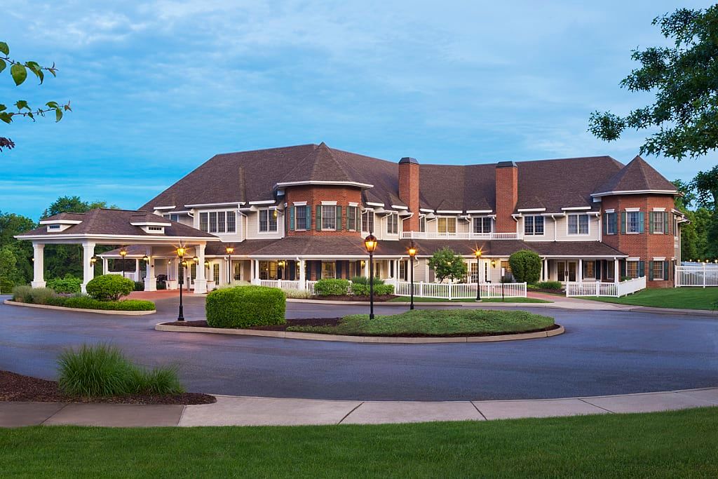 A large residential building with a circular driveway and well-maintained landscaping at dusk.