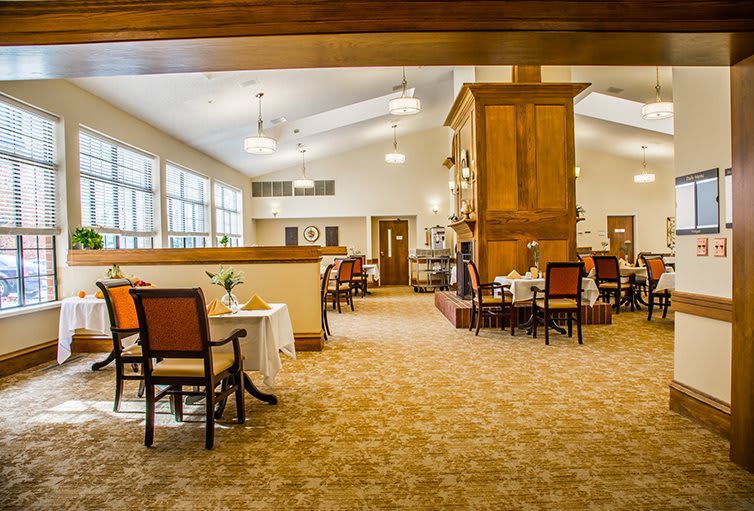 A spacious dining room with neatly arranged tables and chairs, featuring large windows and warm lighting.