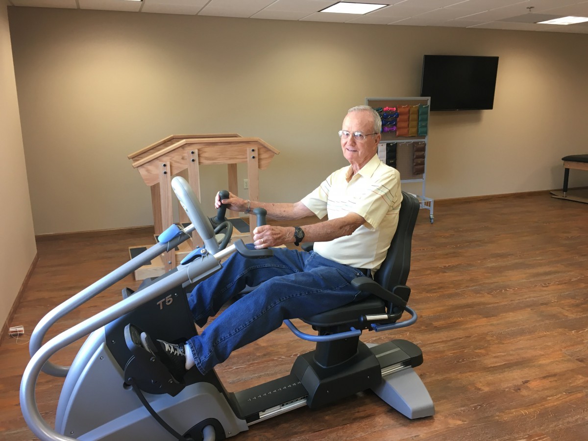 A senior person exercising on a recumbent bike indoors.