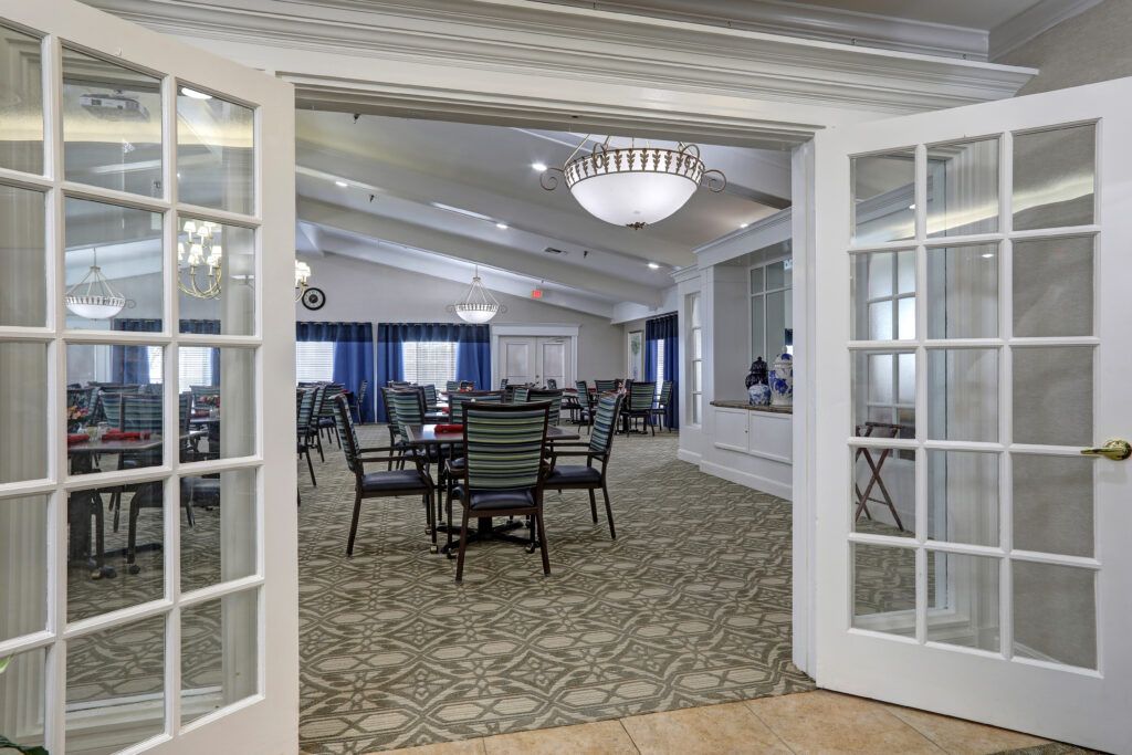 A spacious dining room with elegant chandeliers, featuring multiple tables and chairs, accessible through glass doors.