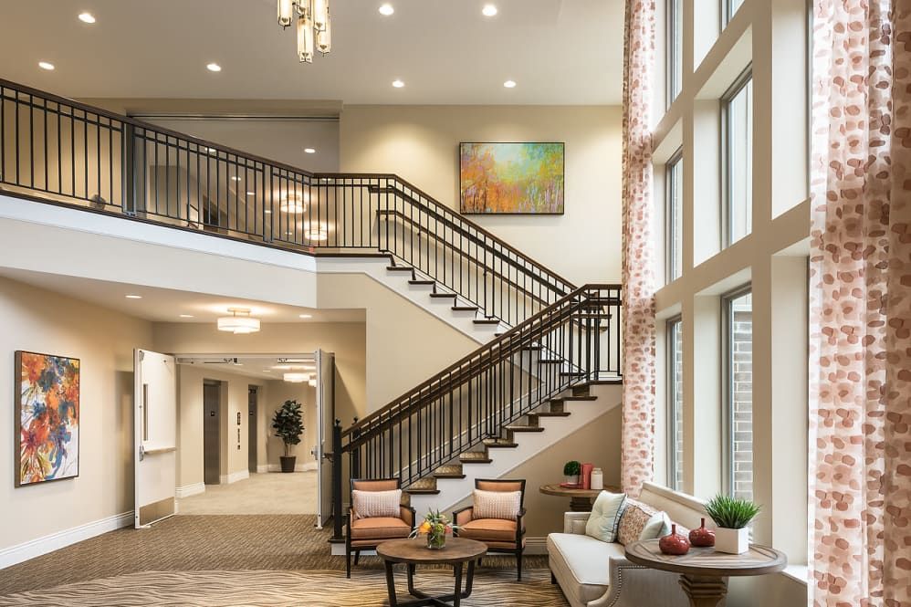 A modern lobby featuring a grand staircase with elegant lighting, comfortable seating, and large windows.