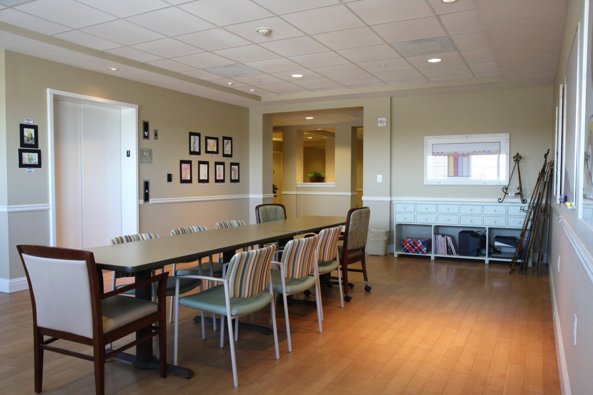 A well-lit dining area with a long table and multiple chairs, decorated with framed pictures on the wall and featuring a wooden floor.