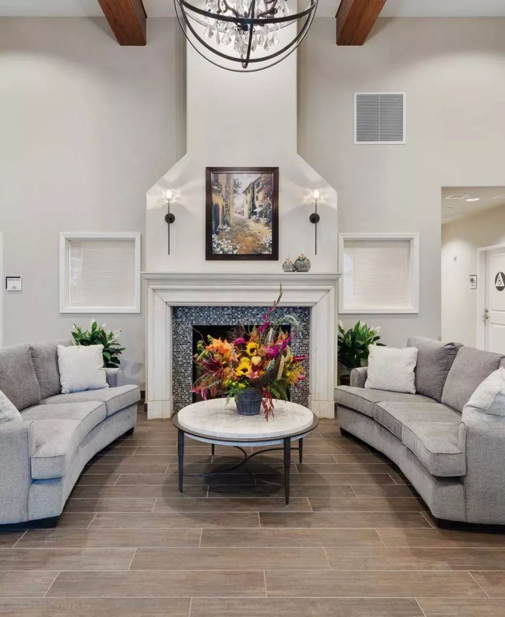 A modern living room featuring a fireplace, curved sofas, and a centerpiece coffee table adorned with flowers.