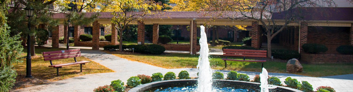 A fountain surrounded by autumn trees and a brick walkway.