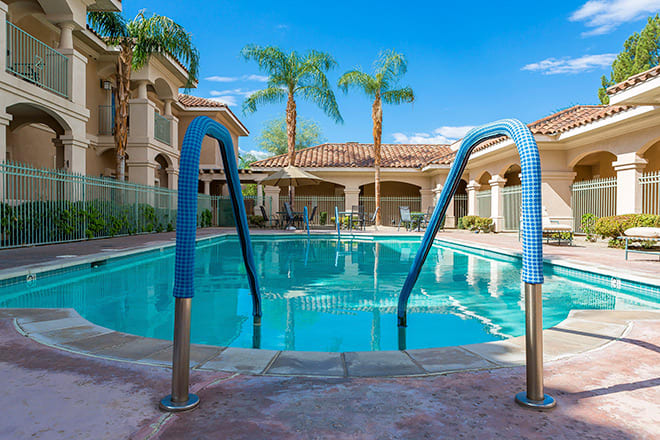 A serene outdoor swimming pool surrounded by palm trees and resort-style buildings, ideal for a relaxing vacation.
