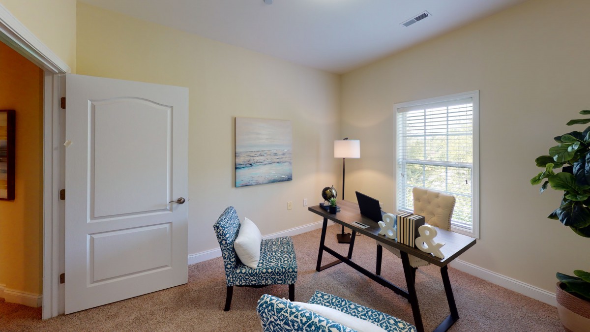 A cozy home office setup with a desk, chairs, and a bright window.