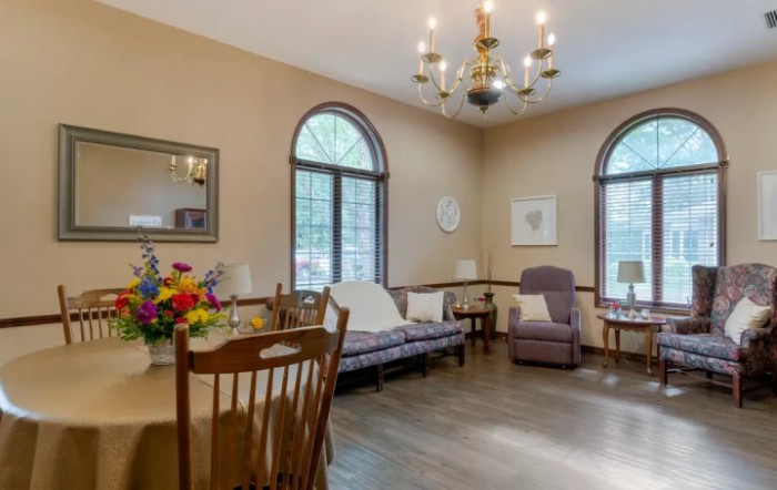 A cozy living room featuring a dining table with flowers, comfortable seating, and large arched windows.