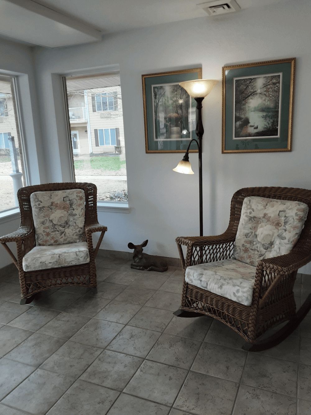 A cozy living room corner with two wicker chairs, a standing lamp, and wall art.