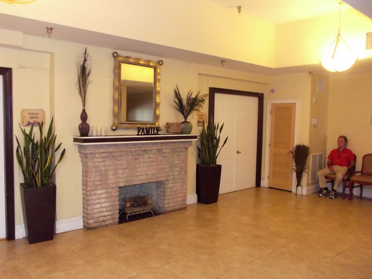 A cozy living room with a brick fireplace, decorative mirror, and potted plants.