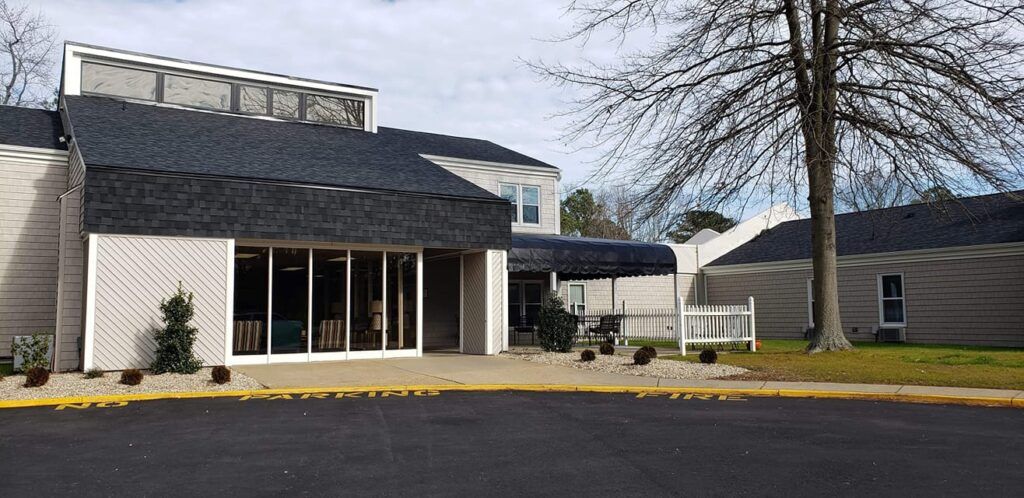 A commercial building with large windows and an awning, adjacent to a parking lot and a tree.
