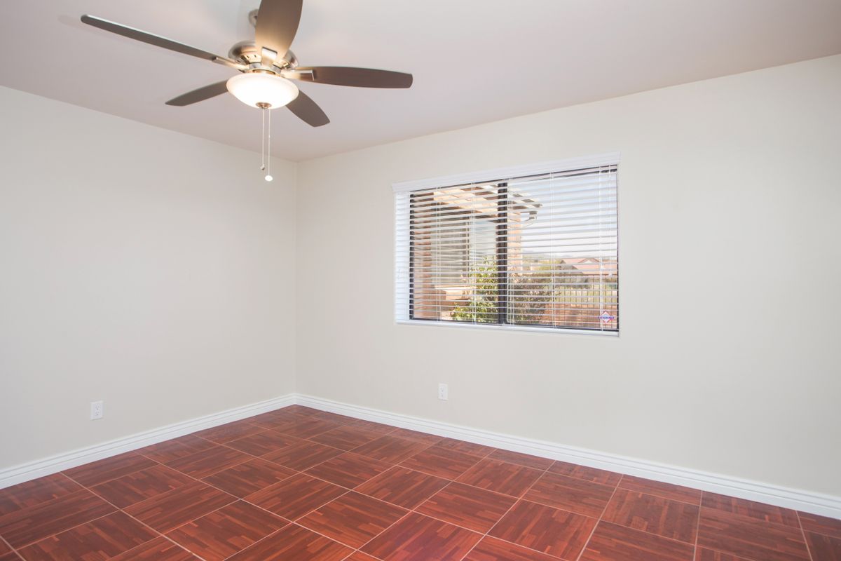 An empty room with a ceiling fan, tiled floor, and a window with blinds letting in natural light.