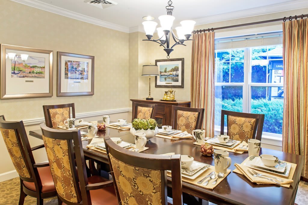 A beautifully set dining room with elegant chairs, a chandelier lighting the area, and large windows allowing natural light in.