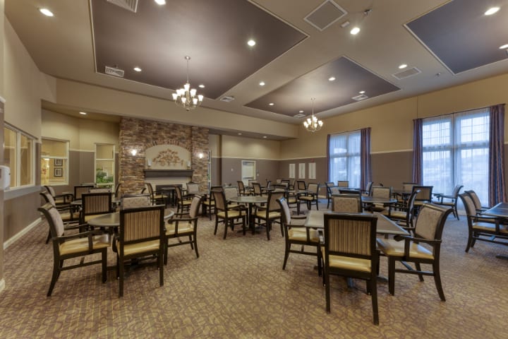 A spacious and elegantly designed dining room with multiple tables and chairs, featuring a brick fireplace and chandeliers.
